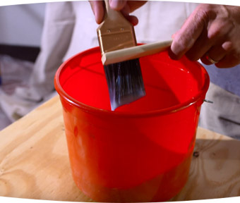 Person cleaning off a paint brush over a red bucket