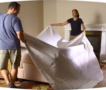 Two people covering furniture with tarp in preparation for painting