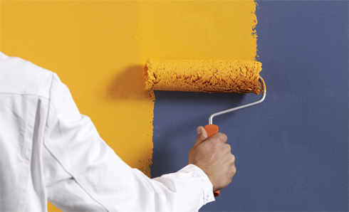 Person rolling yellow paint on a dark gray wall