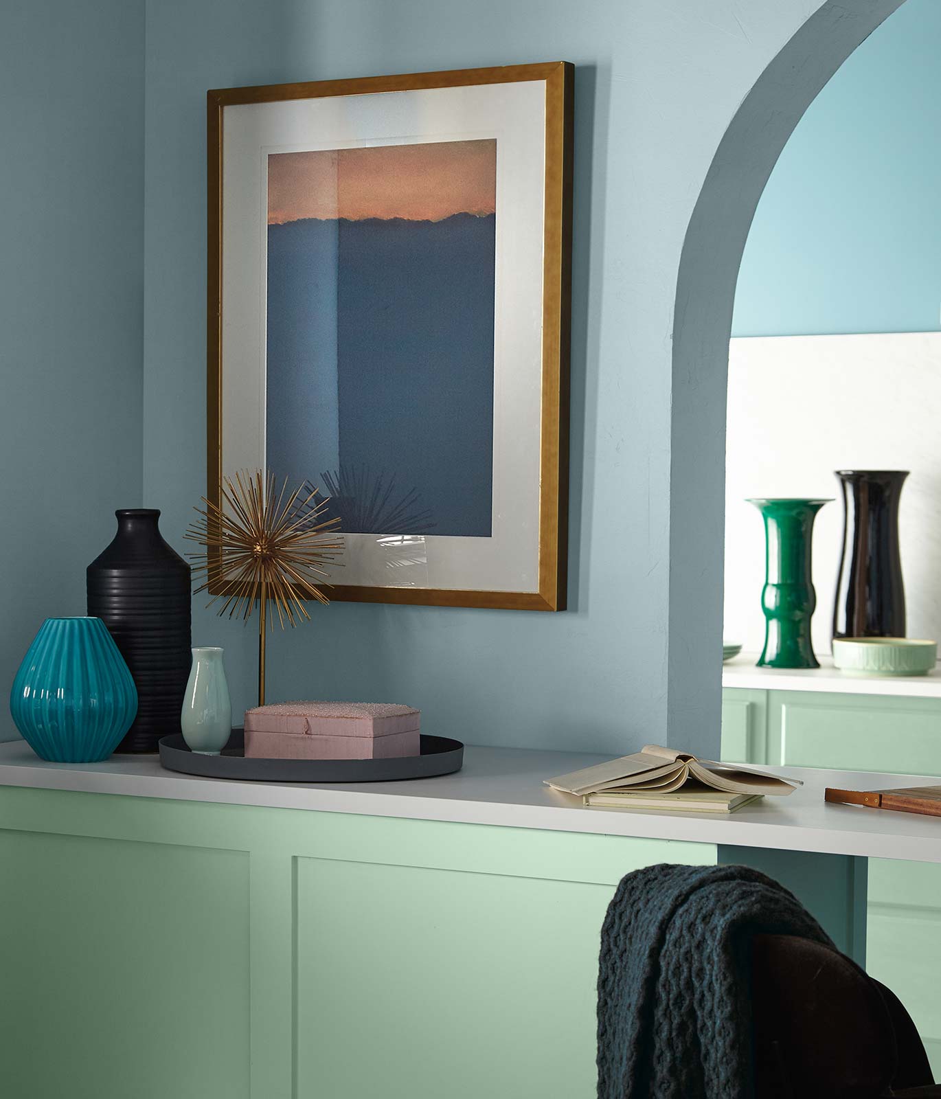 A buffet table painted in soft, subtle green with a white counter top sitting against a blue painted wall.